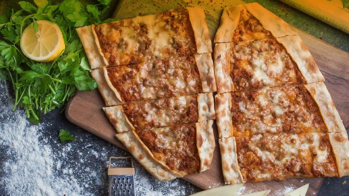 Minced meat pide Boat-shaped Turkish pide with minced meat topping, sliced into strips with parsley and lemon