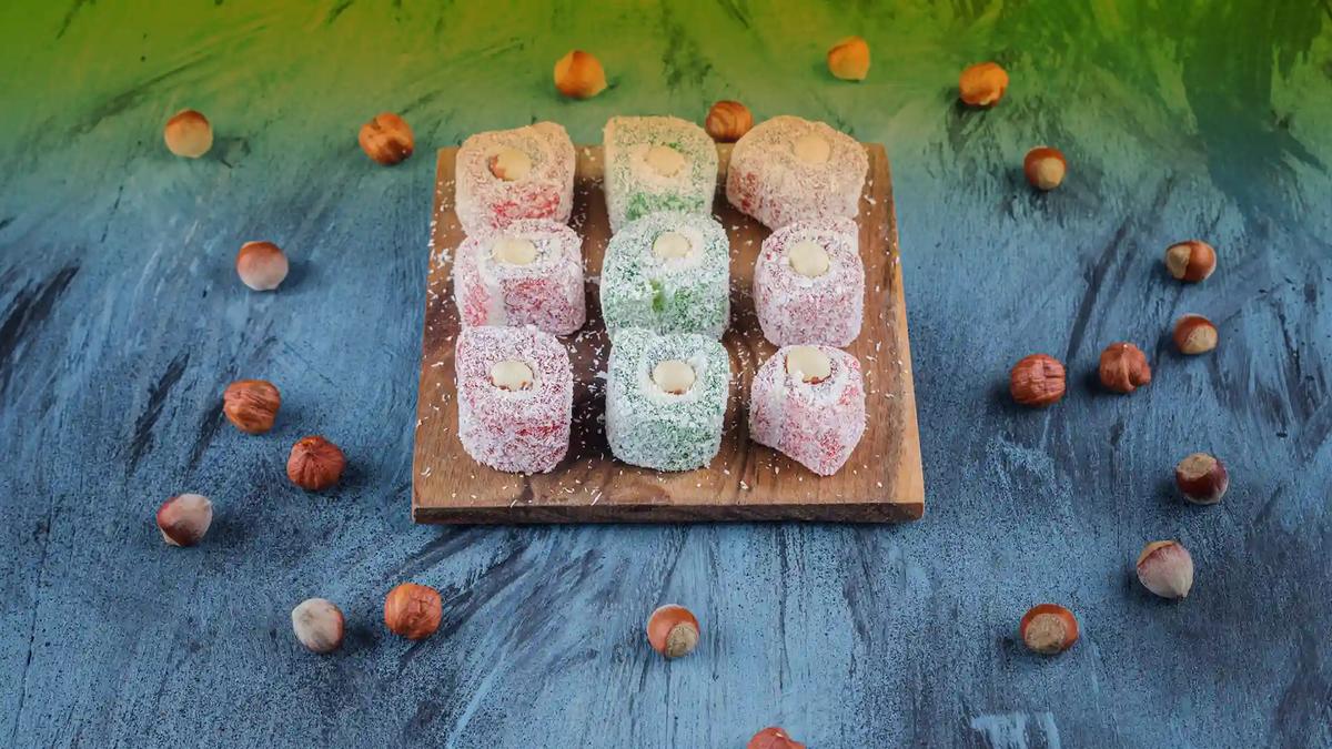 Rolled Turkish delight with hazelnuts Coconut-dusted Turkish delight rolls on a wooden board surrounded by hazelnuts